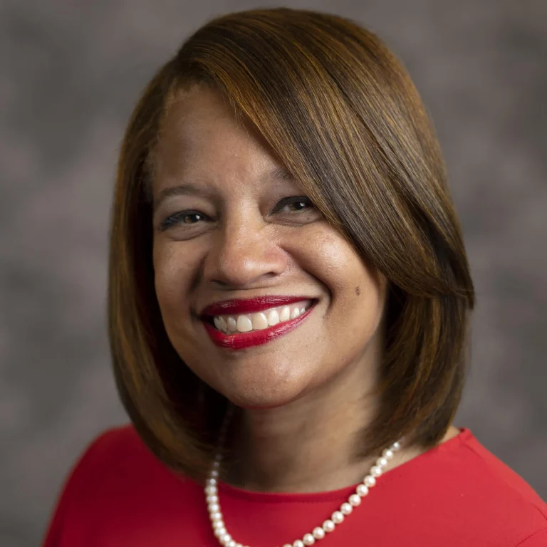 A black woman with straight brown hair wearing red shirt and string of pearls